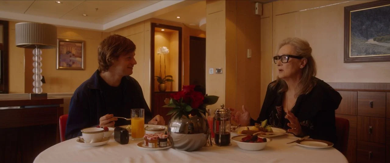 Let Them All Talk movie still: medium — A luxury hotel room with wood-paneled walls and a table set for breakfast. A young man and an older woman…