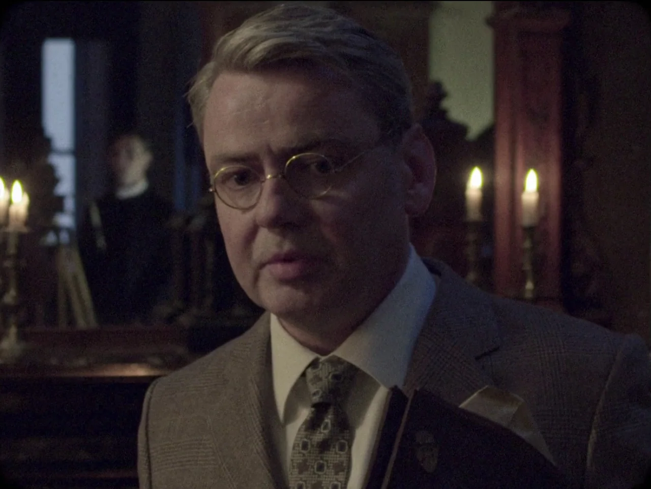 The Devil’s Doorway (2018) movie still: closeup — A dimly lit room with antique wooden furniture and ambient candlelight in the background. A…