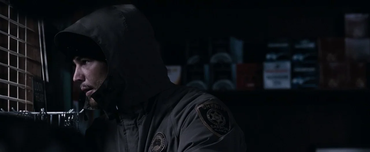30 Days of Night (2007) movie still: medium — A dimly lit room with shelves of blurred supplies in the dark background. A man wearing a sheriff…