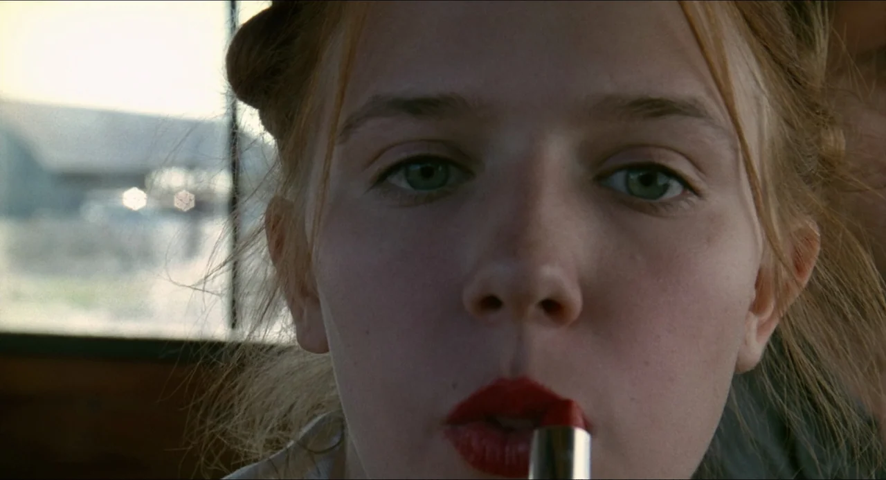 Lolita (1997) movie still: closeup — A close view inside a vehicle with daylight visible through the window. A young woman with red lipstick looks…