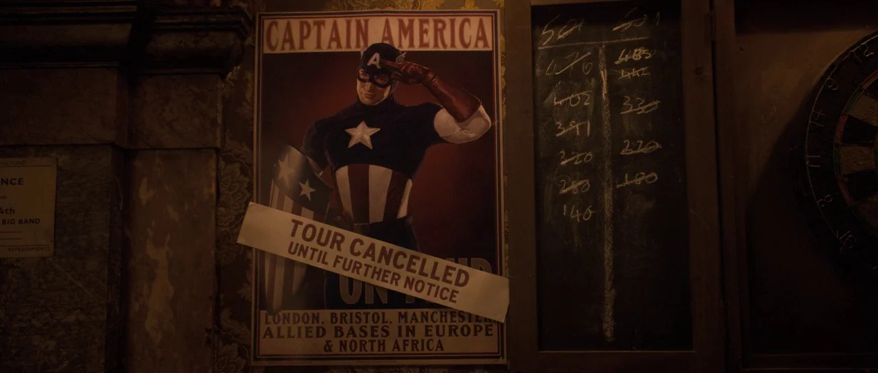Captain America: The First Avenger (2011) movie still: medium — A dark, dimly lit wall features a vintage Captain America propaganda poster. A…