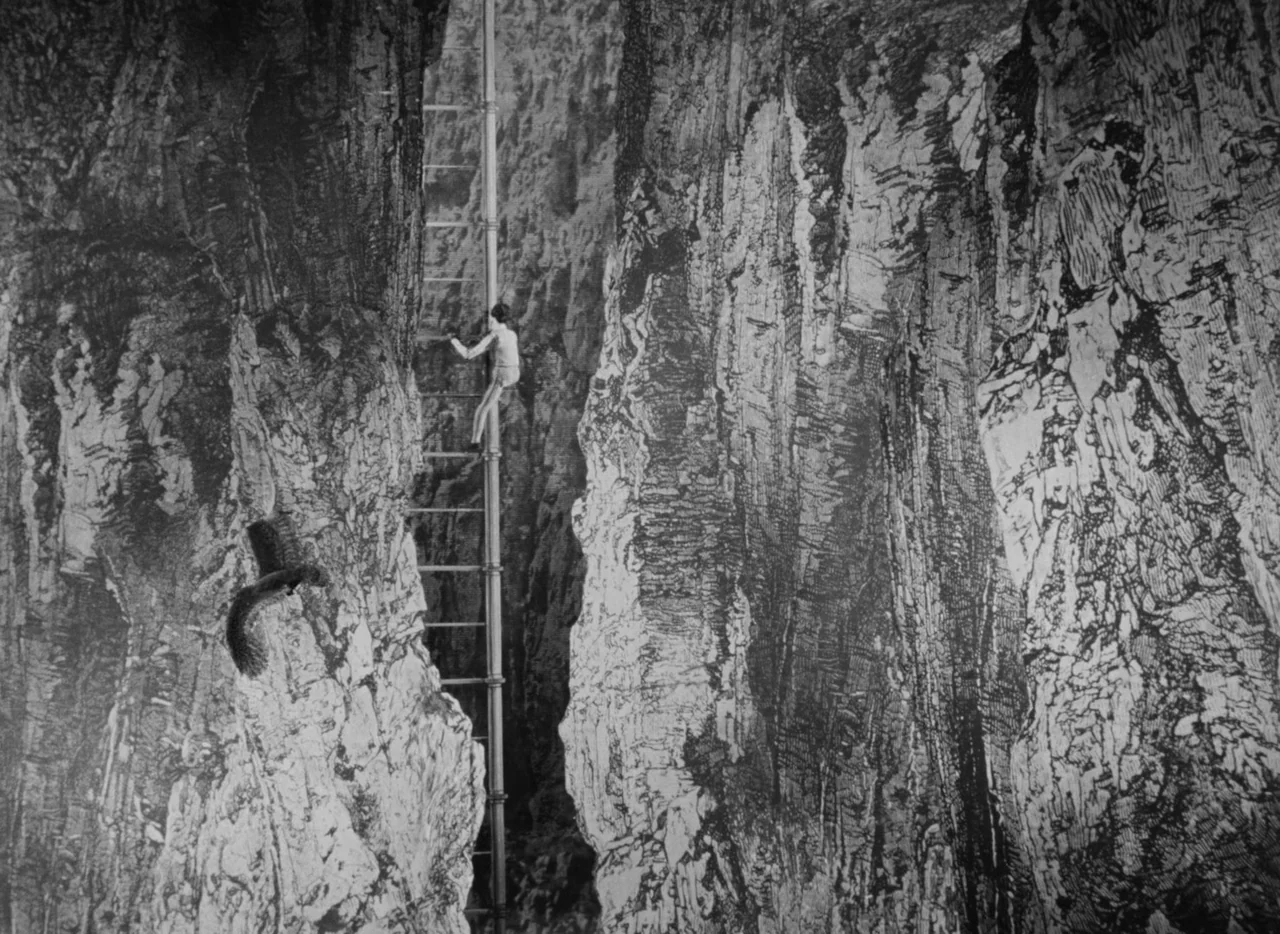 Invention For Destruction (1958) movie still: wide — Two textured, highly detailed rock walls flank a narrow central gap. A person climbs a long,…