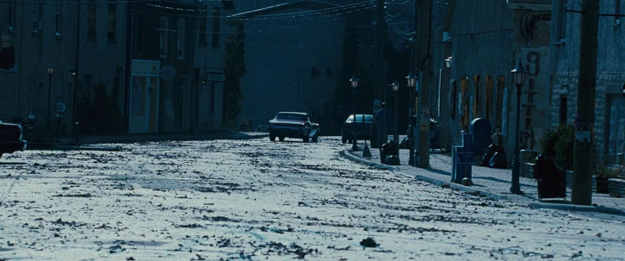 Dead Silence (2007) movie still: establishing — A dimly lit street at night is covered in scattered debris and fallen leaves. A vintage muscle car…