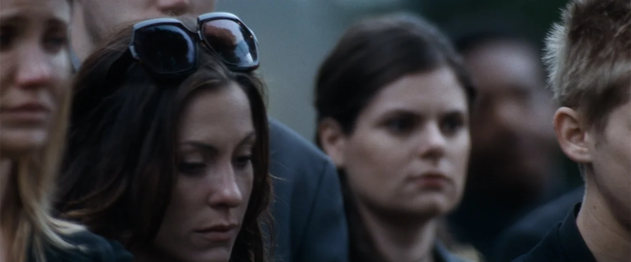 My Sister's Keeper (2023) movie still: medium — A group of people dressed in dark clothing stand together outdoors in daylight. They are gathered in…