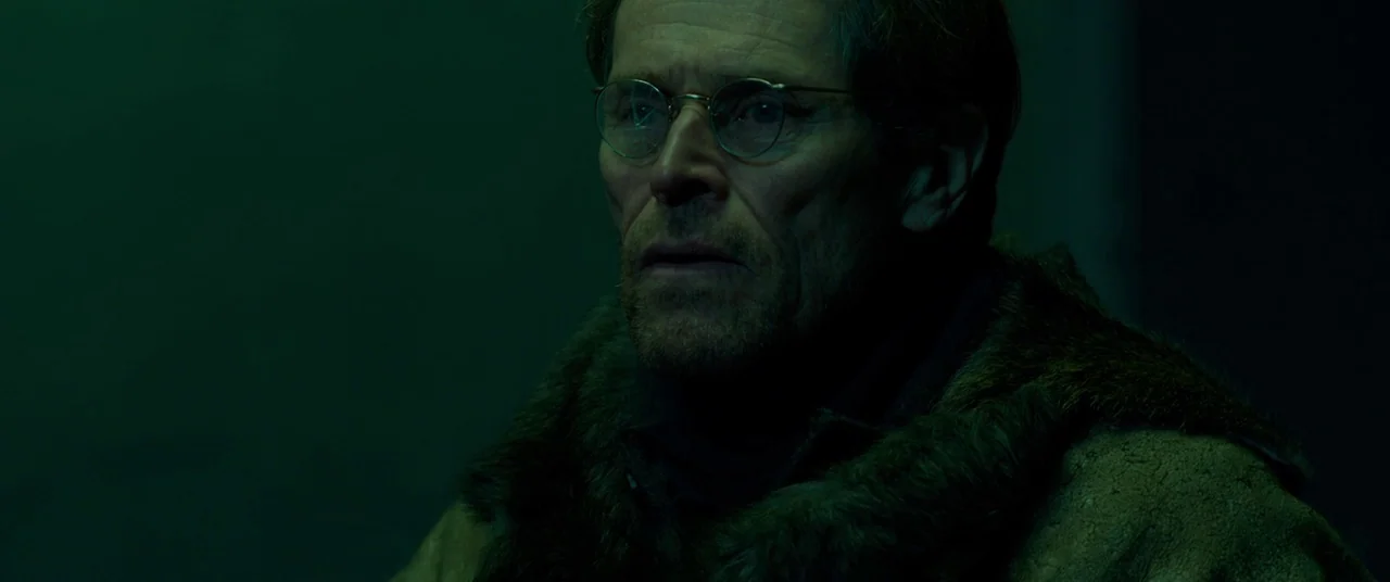 Siberia (2019) movie still: closeup — A man in a thick fur-trimmed coat stands within a dark room. The subject looks forward under a low green light.
