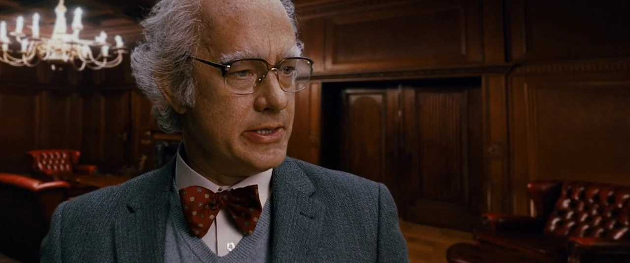 Cloud Atlas (2012) movie still: medium — An wood-paneled room features leather furniture and an overhead chandelier in the background. A man with…