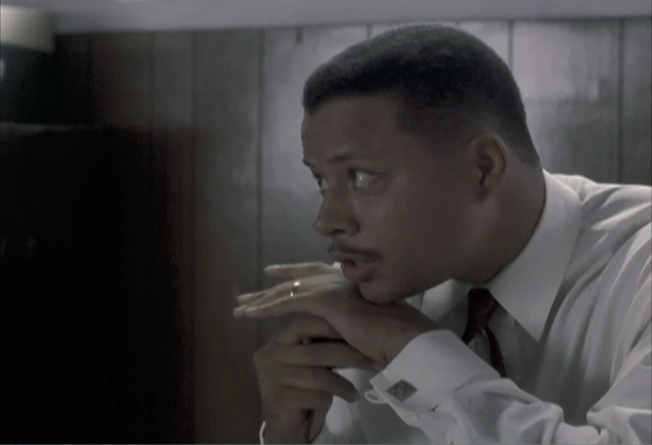 Boycott (2001) movie still: medium — A person sits in a room with wood-paneled walls in the background. The man gazes toward the side while resting…