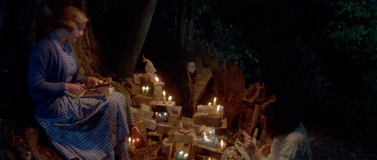 Heavenly Creatures (1994) movie still: medium — Two girls sit by a pile of bricks arranged like an altar in woods. They read small books illuminated…