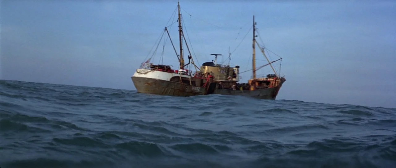 For Your Eyes Only (1981) movie still: wide — A rusted commercial fishing vessel sits on the surface of a choppy ocean. The sky above is a uniform…