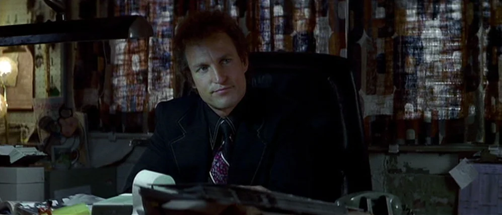 The People vs. Larry Flint (1996) movie still: medium — A dark office setting features a cluttered desk and patterned blinds in the background. A…