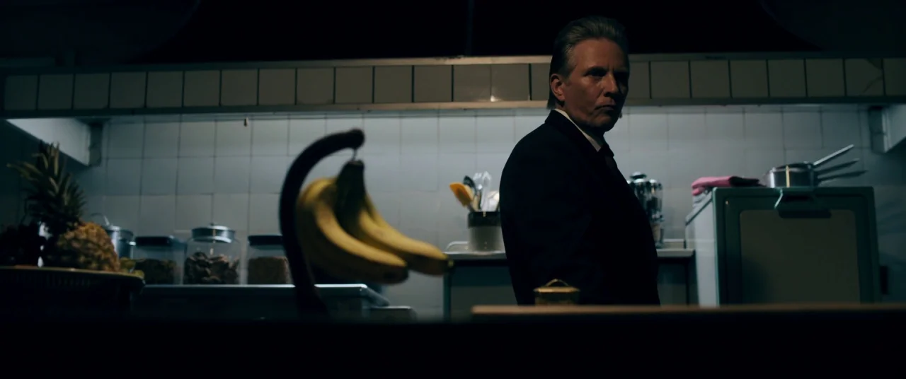 Ready or Not (2019) movie still: medium — A dimly lit room features white tiled walls and assorted countertop storage containers. A man in a dark…