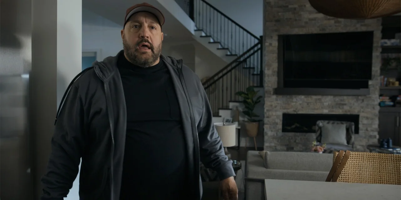Playdate (2025) movie still: medium — A modern open-plan interior features a stone fireplace and dark metal staircase railings. A middle-aged man in…