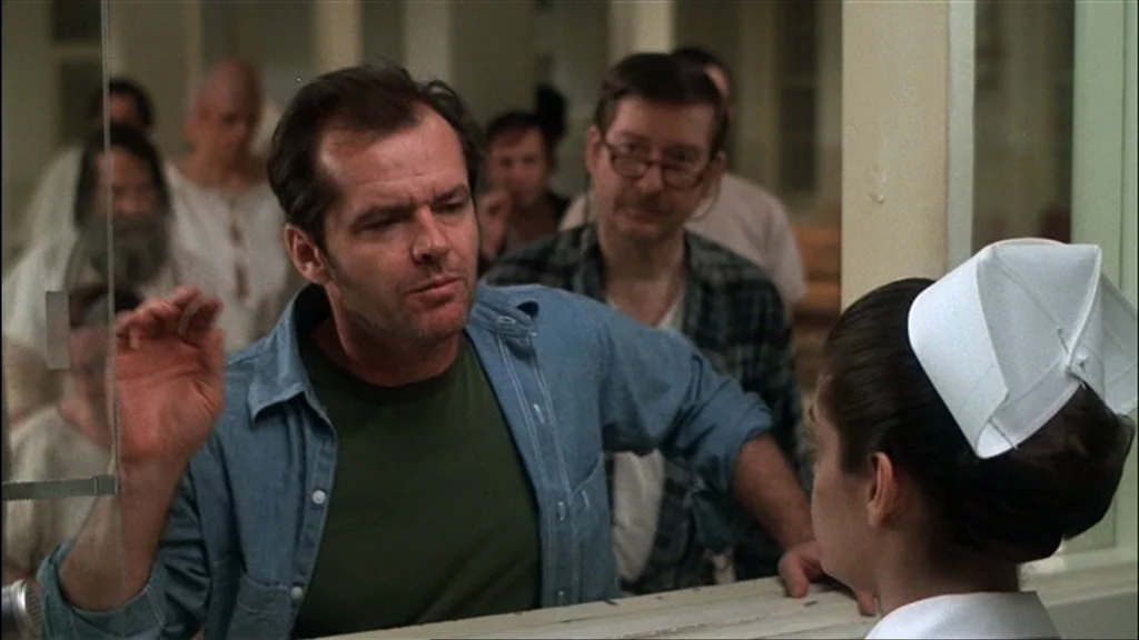 One Flew Over the Cuckoo's Nest (1975) movie still: medium — A clinical, brightly lit medical environment features a clear glass partition and…
