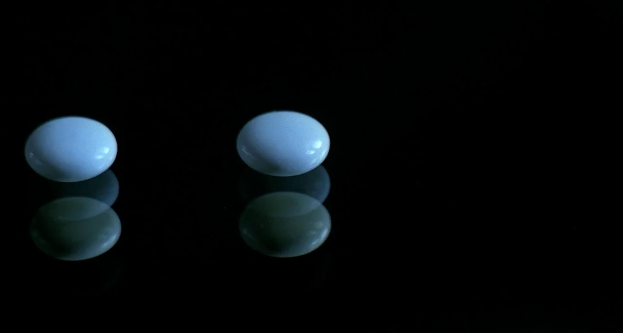 Tenebre (1982) movie still: closeup — Two white circular pills sit on a highly reflective black surface. The objects are mirrored directly beneath…