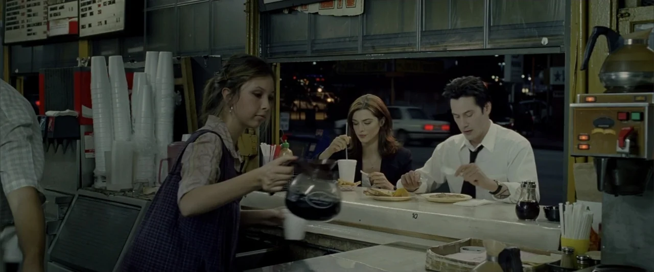 Constantine (2005) movie still: medium — A classic diner interior at night viewed from behind a long service counter. A waitress serves coffee to a…