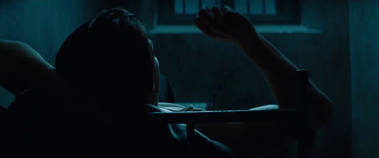 Mission: Impossible – Ghost Protocol (2011) movie still: medium — A dimly lit room contains a bed frame positioned beneath a small barred window. A…