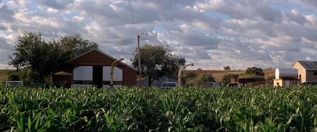 Silent Light (2007) movie still: wide — A rural farm with a large cornfield in the foreground and barn buildings behind. The sky above is filled…