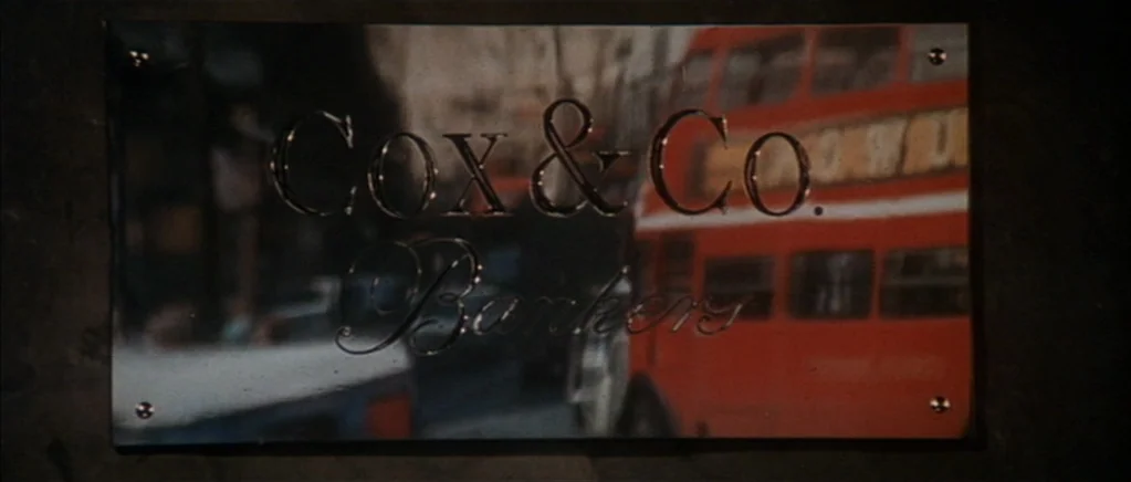 The Private Life of Sherlock Holmes movie still: closeup — A polished metal sign engraved with text is mounted to a dark wall. A red London…