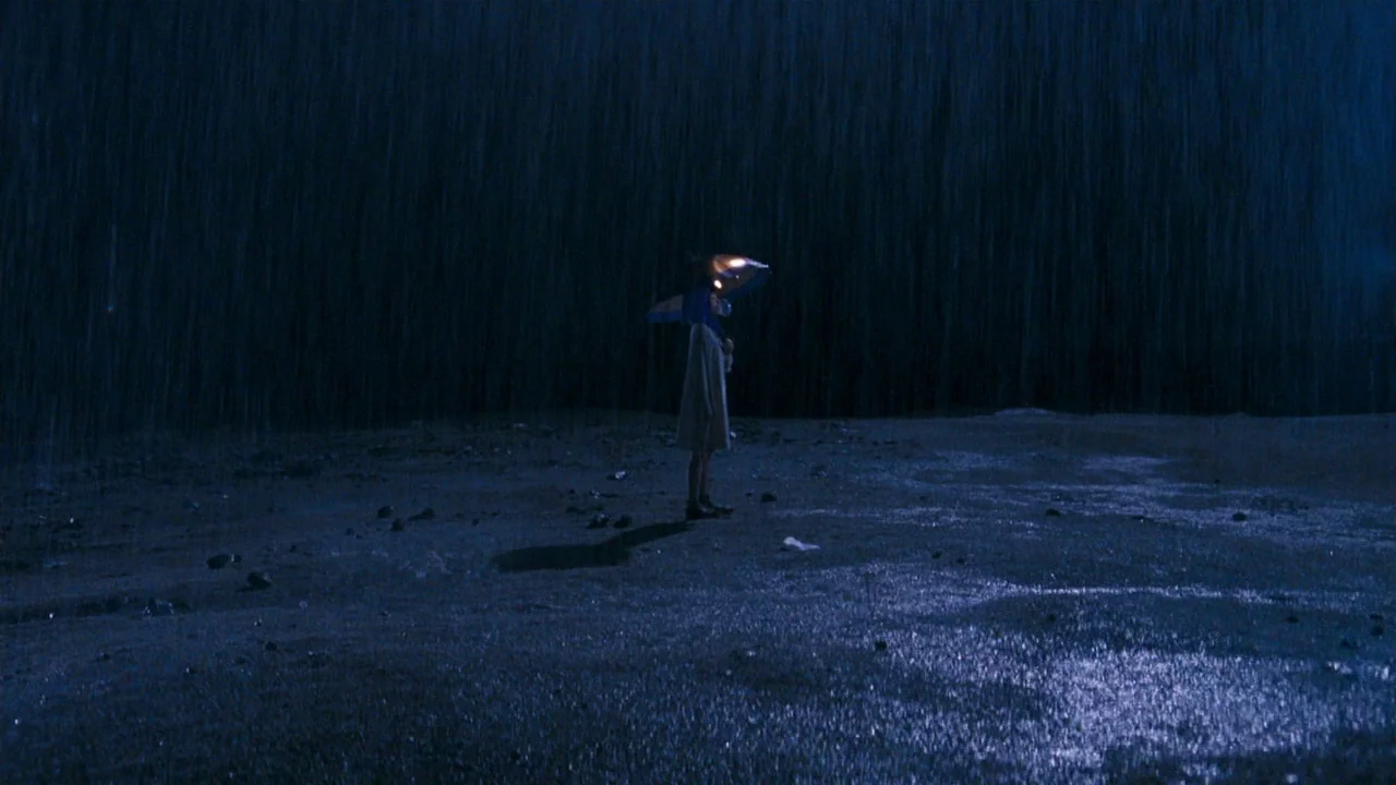 I’m A Cyborg, But That’s Okay (2006) movie still: wide — An open expanse of wet, dark ground is saturated by a heavy nighttime downpour. A single…