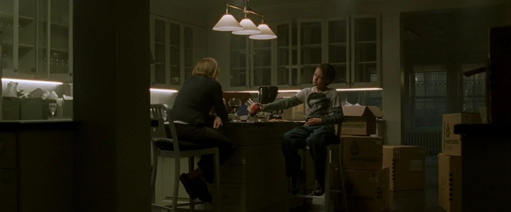 Panic Room (2002) movie still: wide — A residential room contains cardboard packing boxes on the floor during a move. A young boy and a woman sit at…