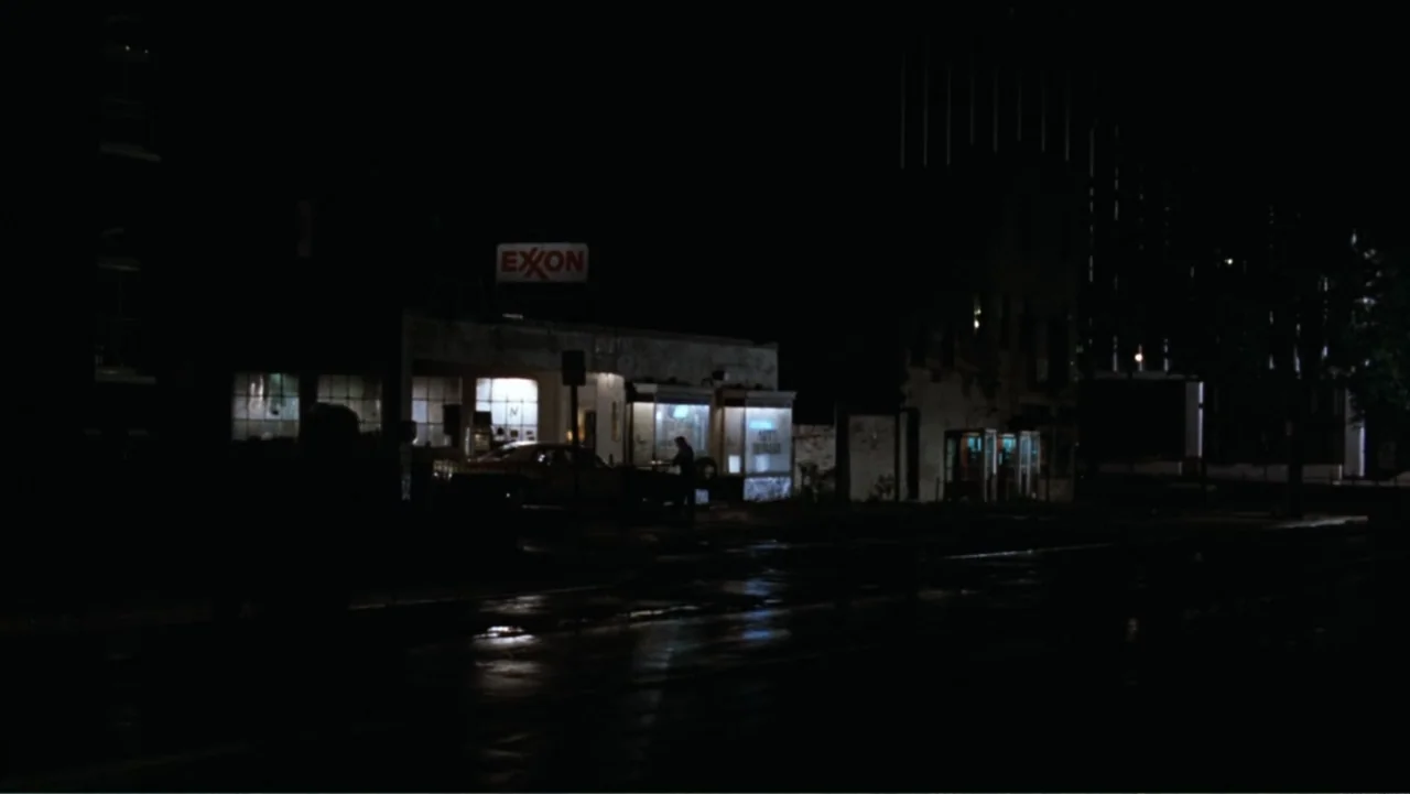 All the President's Men (1976) movie still: wide — An Exxon service station at night features bright interior lights against deep darkness. A lone…