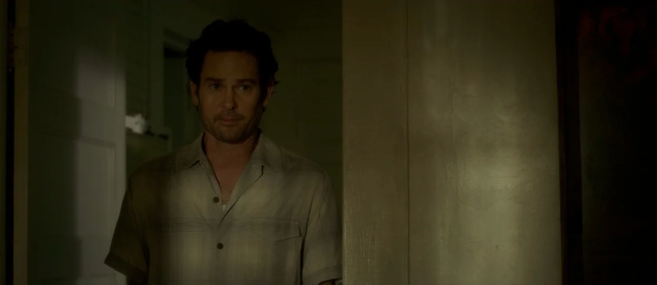 Gerald’s Game (2017) movie still: medium — A man stands in the threshold of an interior room with muted walls. The man looks ahead while framed by a…