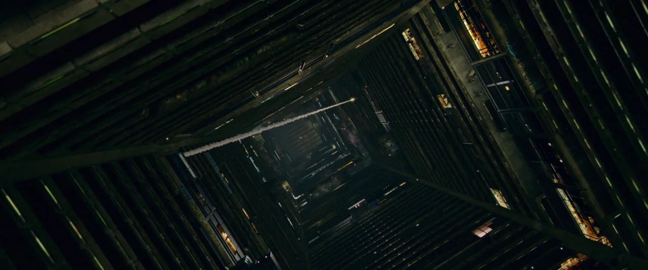 Dredd (2012) movie still: establishing — A dark, vertical shaft of a mega-structure building at night with infinite levels. A thin white streak of…