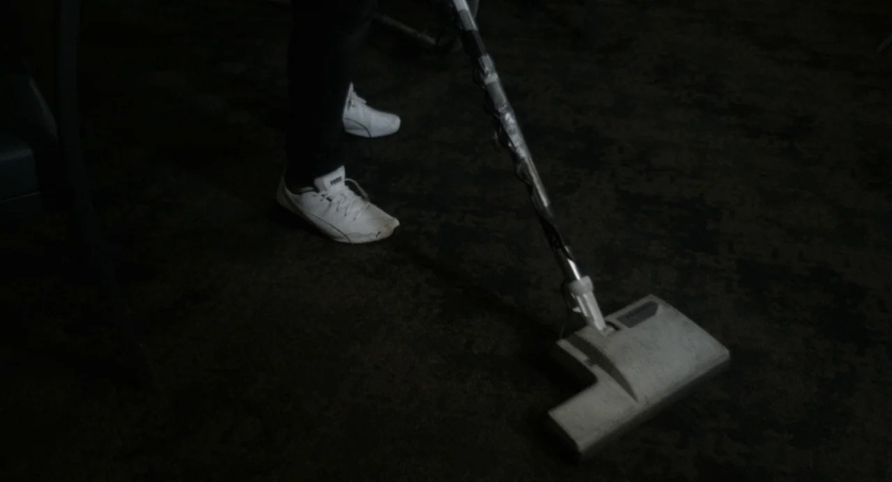Happer’s Comet (2022) movie still: medium — A darkened interior space features a plush carpet floor with indistinct patterns. A person in dark…