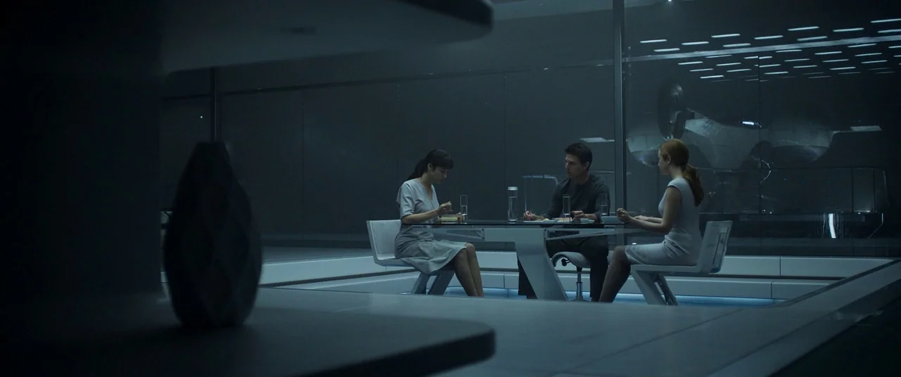 Oblivion (2013) movie still: wide — A minimalist, glass-enclosed futuristic room features a sleek table and integrated recessed lighting. Two women…
