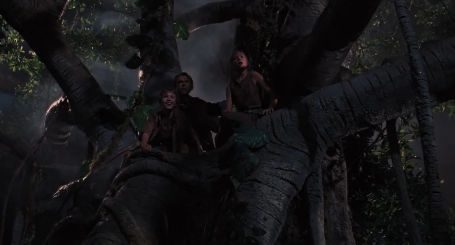 Jurassic Park (1993) movie still: medium — Three people huddle together on the thick, textured limbs of a large tree. They peer upward through the…