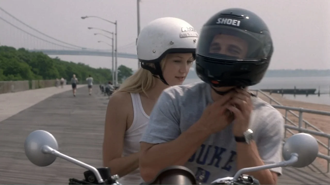 How to Lose a Guy in 10 Days (2003) movie still: medium — A sunny coastal boardwalk stretches towards a distant suspension bridge. A man wearing a…