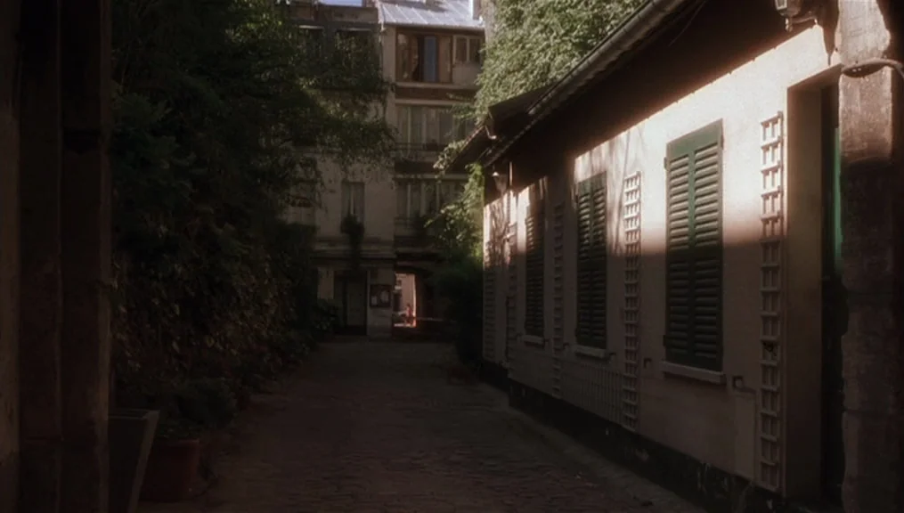 Before Sunset (2004) movie still: establishing — A narrow stone-paved passage sits between a tall apartment building and a lower structure. Thick…
