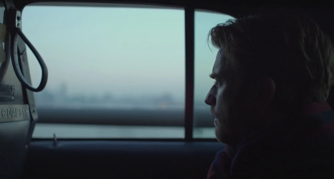 Beginners (2010) movie still: closeup — The interior of a taxi cabin features a dark door panel and a handle. A man looks out the window at a hazy,…