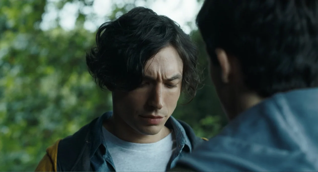 The Flash (2023) movie still: closeup — A dense patch of green foliage creates a natural background outdoors during the day. A young man with dark…