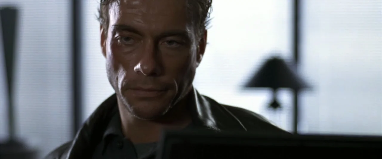 Maximum Risk (1996) movie still: closeup — An office interior features a subject seated near a window with horizontal blinds. A man with short dark…