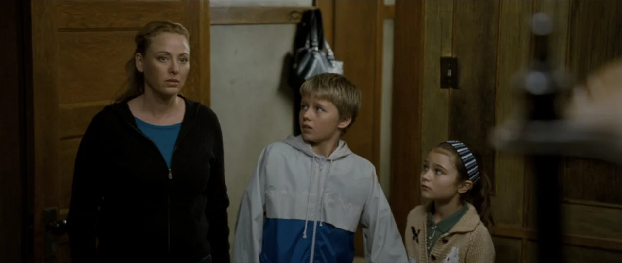 The Haunting in Connecticut (2009) movie still: medium — An interior residential hallway features wooden paneled walls and a door frame. A woman and…