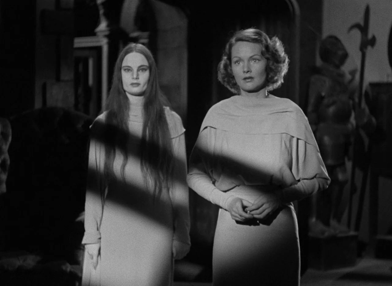 Mark of the Vampire (1935) movie still: medium — An interior space features two women standing in front of a suit of armor. A harsh light casts…