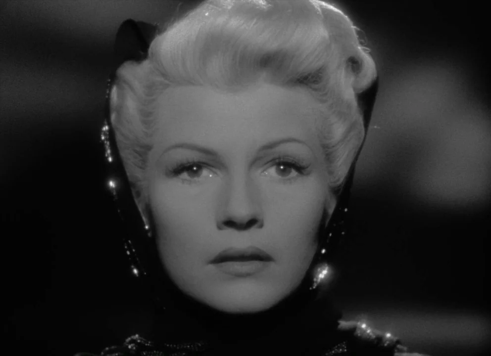The Lady from Shanghai (1947) movie still: closeup — A woman stands against a dark, featureless background with lighting focused on her face. She…