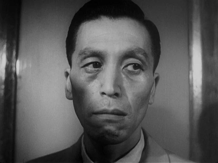Ikiru (1952) movie still: closeup — A close-up shot of an East Asian man inside a dimly lit interior room. The man faces slightly to the right with…