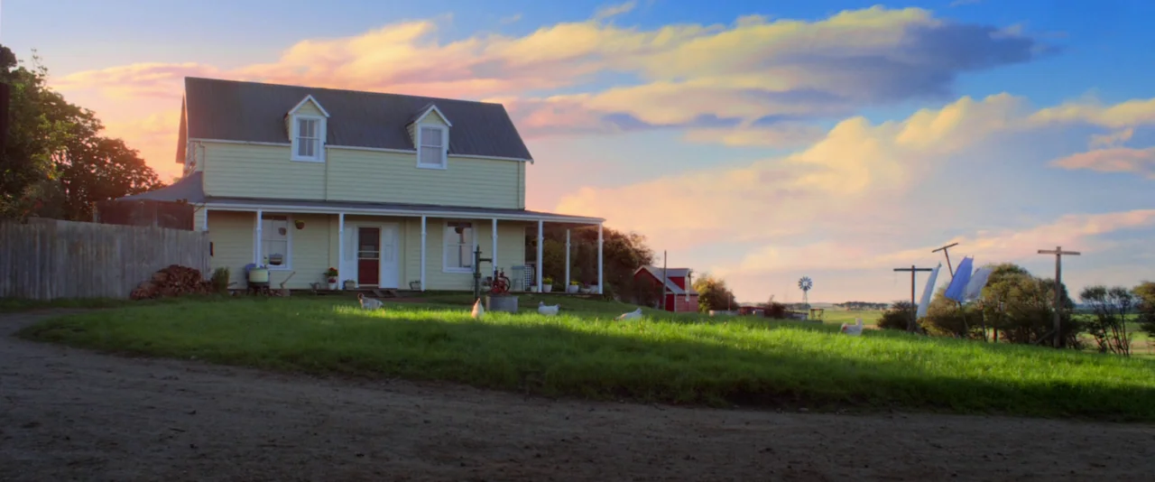Pearl (2022) movie still: establishing — A light-yellow two-story farmhouse with a porch sits in a green rural field. Multiple white chickens wander…