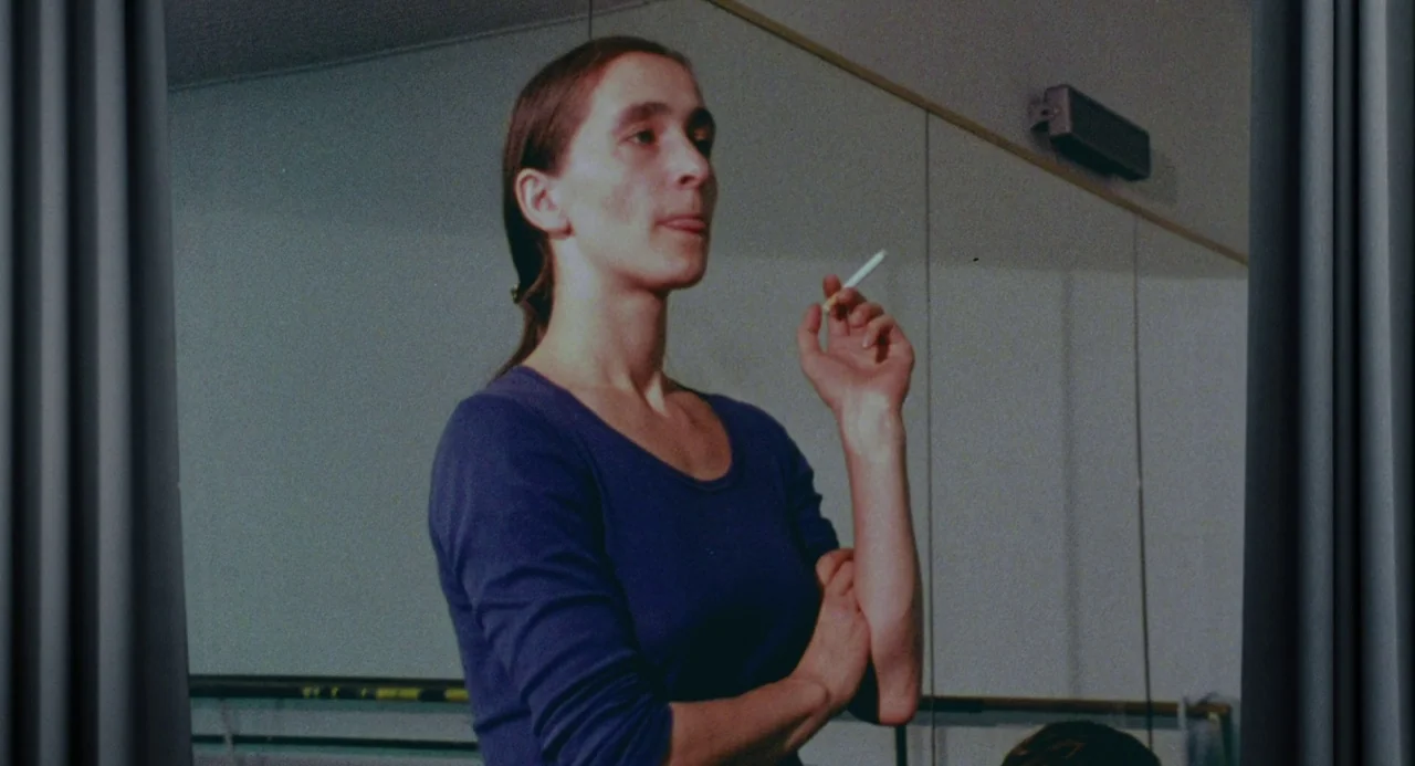 Pina (2011) movie still: medium — A woman stands in a dance studio with large wall-to-wall mirrors. She holds a lit cigarette while standing in…