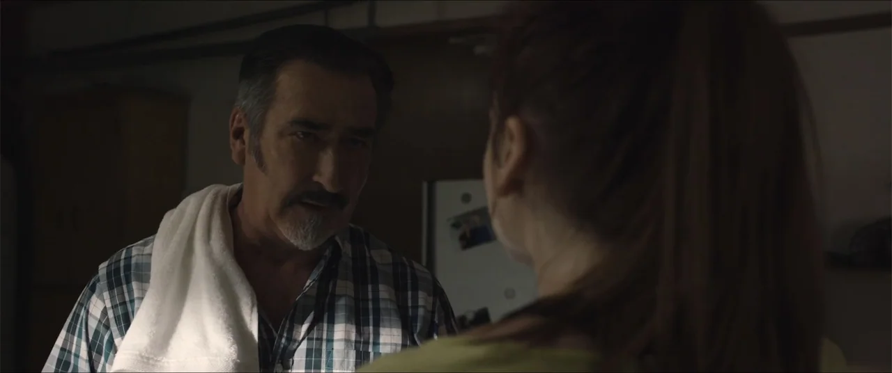 Captive (2020) movie still: medium — An interior kitchen setting featuring a man facing a woman who has her back turned. The man is wearing a plaid…