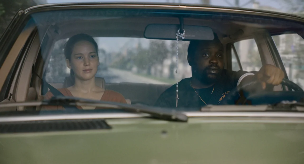 Causeway movie still: medium — A view from inside an older sedan showing the dashboard, windshield, and two passengers. A man drives while a woman…