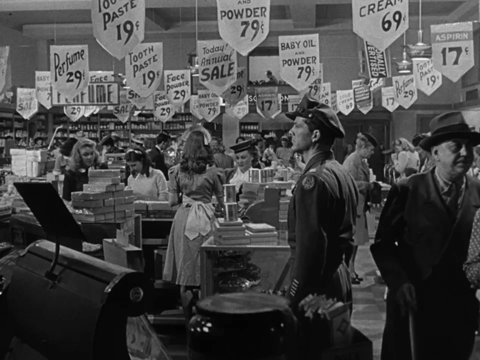 The Best Years of Our Lives (1946) movie still: wide — A crowded 1940s retail interior features numerous hanging price signs for beauty products.…