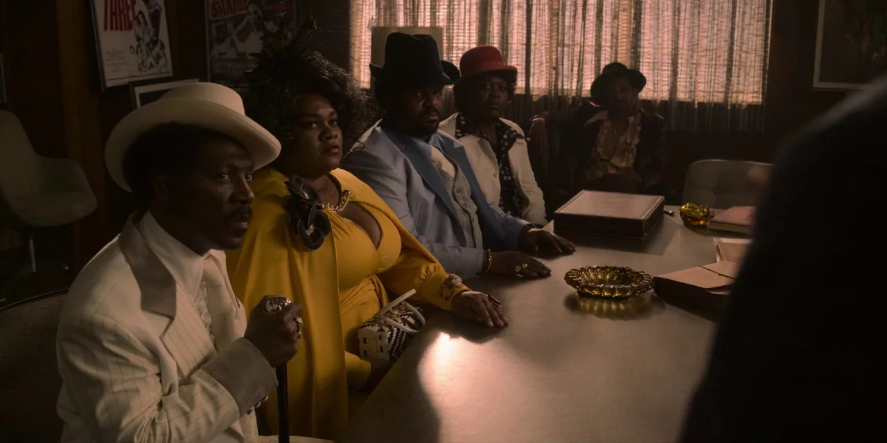 Dolemite Is My Name movie still: medium — A 1970s boardroom features wood-paneled walls and a long conference table. Several people in colorful,…