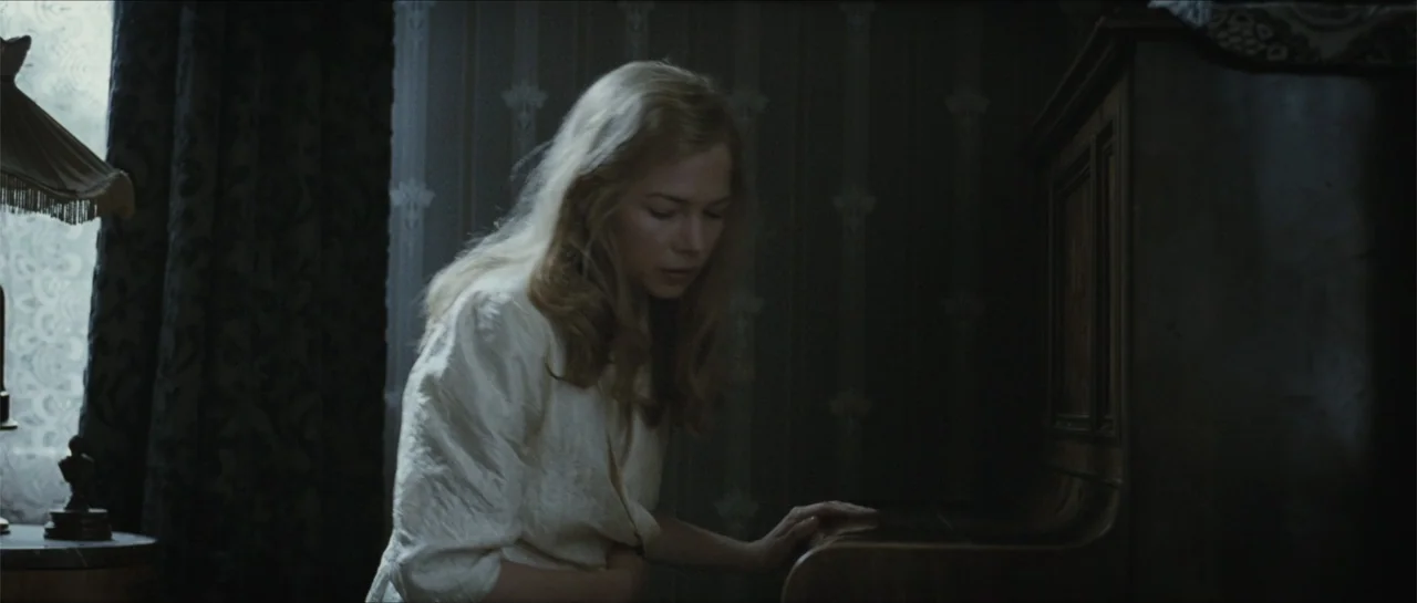 Suite Française (2015) movie still: medium — A dimly lit room features patterned wallpaper and a large wooden piano. A woman stands in front of the…