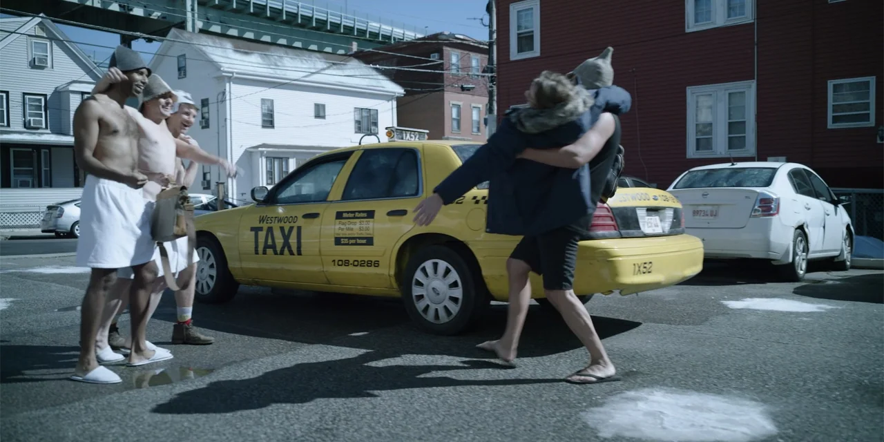 About Fate (2022) movie still: fullbody — A sunny paved lot features a yellow sedan taxi and nearby residential buildings. One man carries a second…