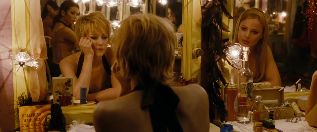 Sucker Punch (2011) movie still: medium — A cluttered backstage dressing room with vanity mirrors framed by rows of incandescent bulbs. A blonde…