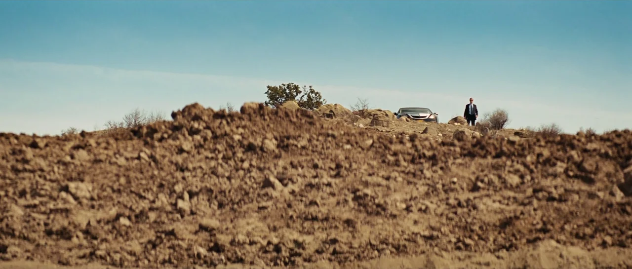 Iron Man 2 (2010) movie still: wide — An arid, rocky desert landscape stretches out with a pile of earth in foreground. A man in a suit stands…