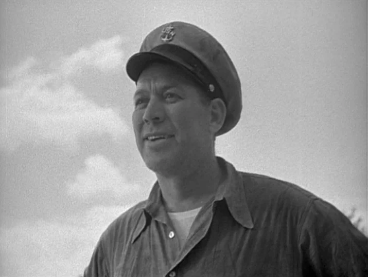They Were Expendable (1945) movie still: medium — A man in a naval uniform stands outdoors against a bright, cloudy sky. He is looking off to the…